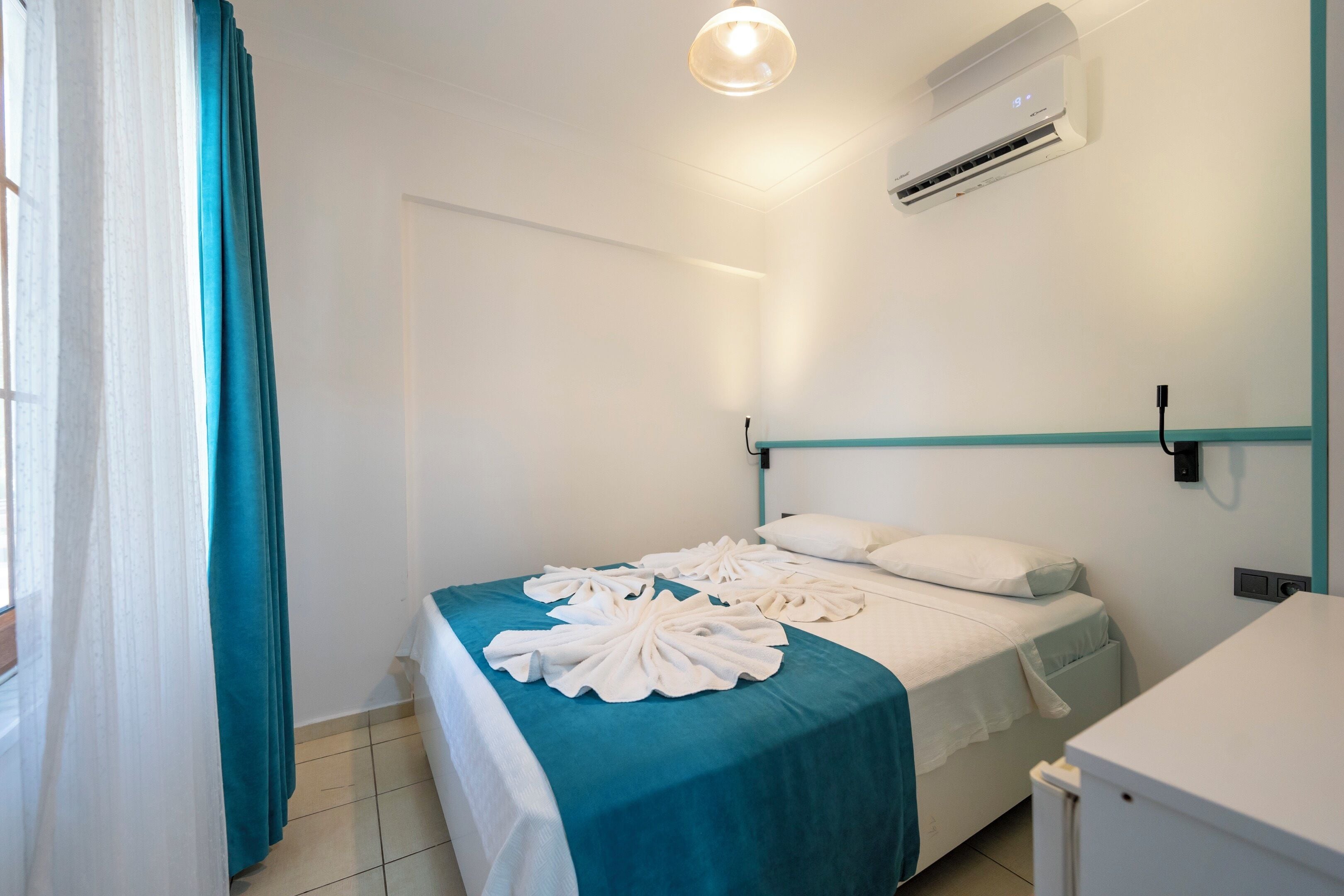 A hotel room with a bed, a desk, and an air conditioning unit.