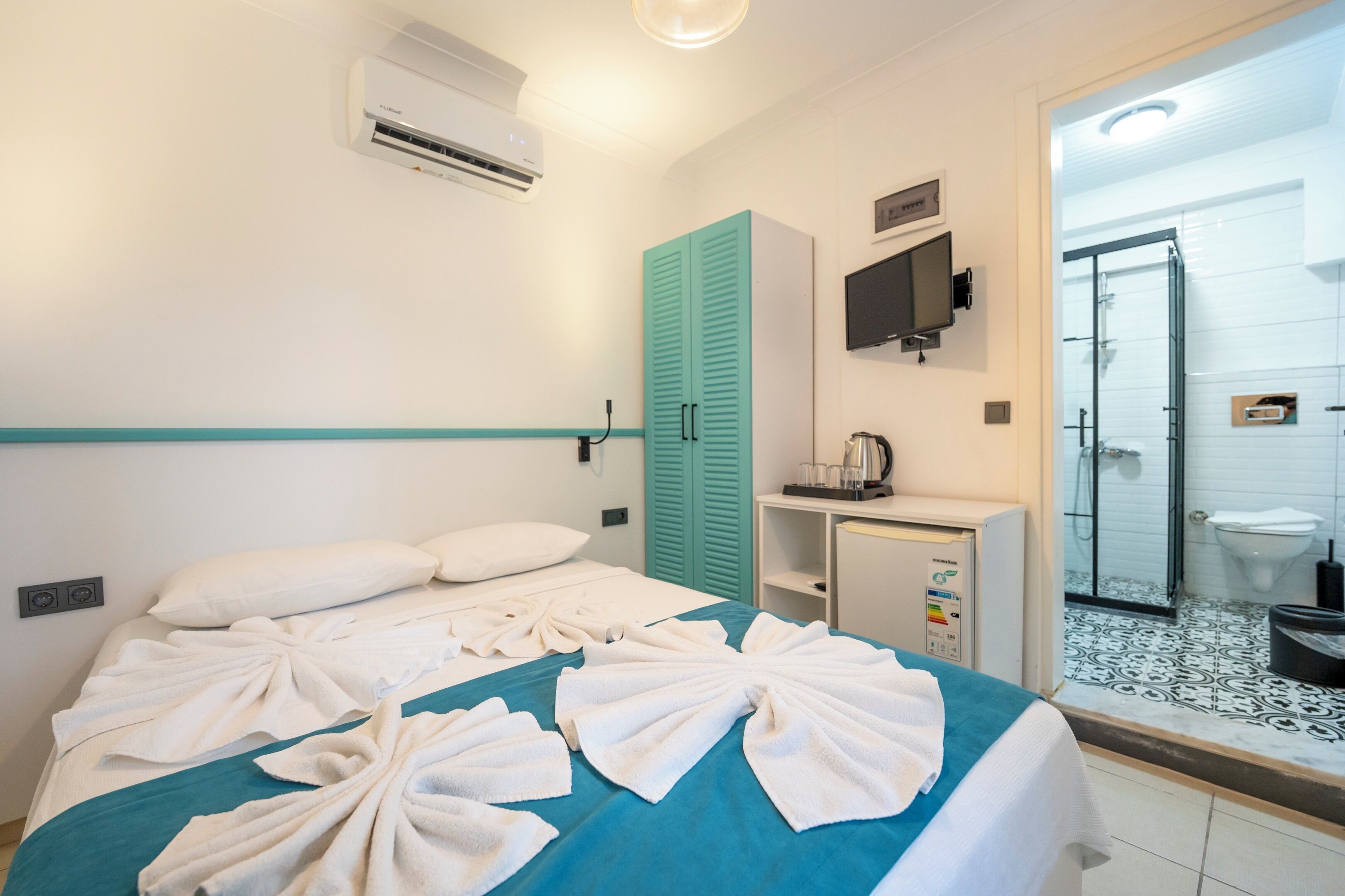 A hotel room with a bed, a minibar, a television, and a bathroom with a shower and toilet.