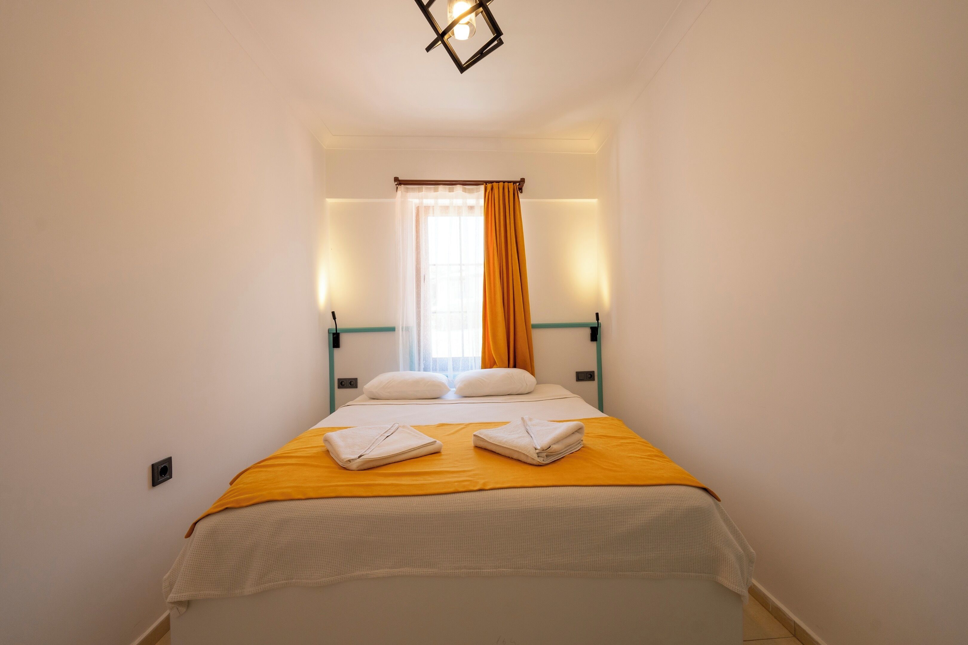Une chambre d’hôtel avec un lit, une fenêtre avec des rideaux et un luminaire fixé au mur.