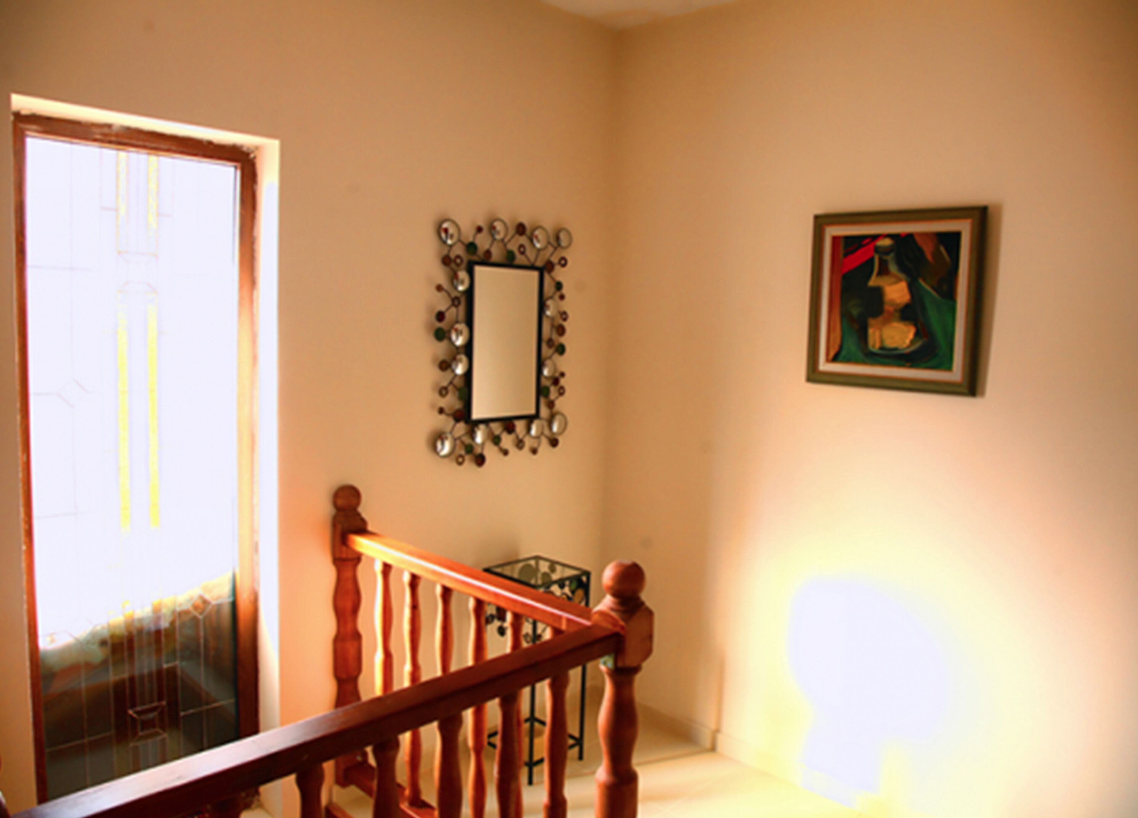Una escalera con barandillas de madera conduce a una plataforma. Un espejo con un marco decorativo cuelga de la pared, y se observa una obra de arte enmarcada en la pared contigua.