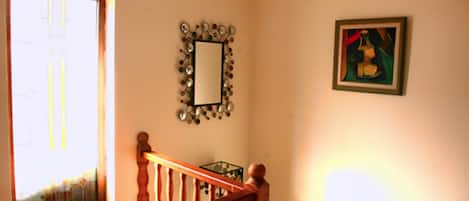 Una escalera con barandillas de madera conduce a una plataforma. Un espejo con un marco decorativo cuelga de la pared, y se observa una obra de arte enmarcada en la pared contigua.