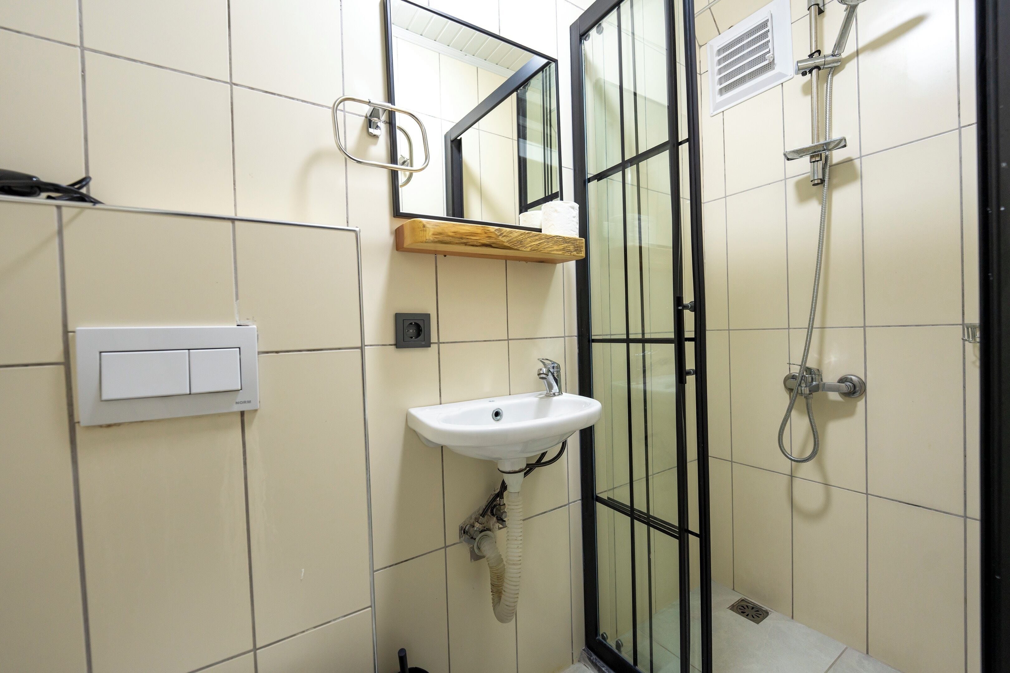 Et badeværelse med hvid vask, spejl, bruser og toilet.