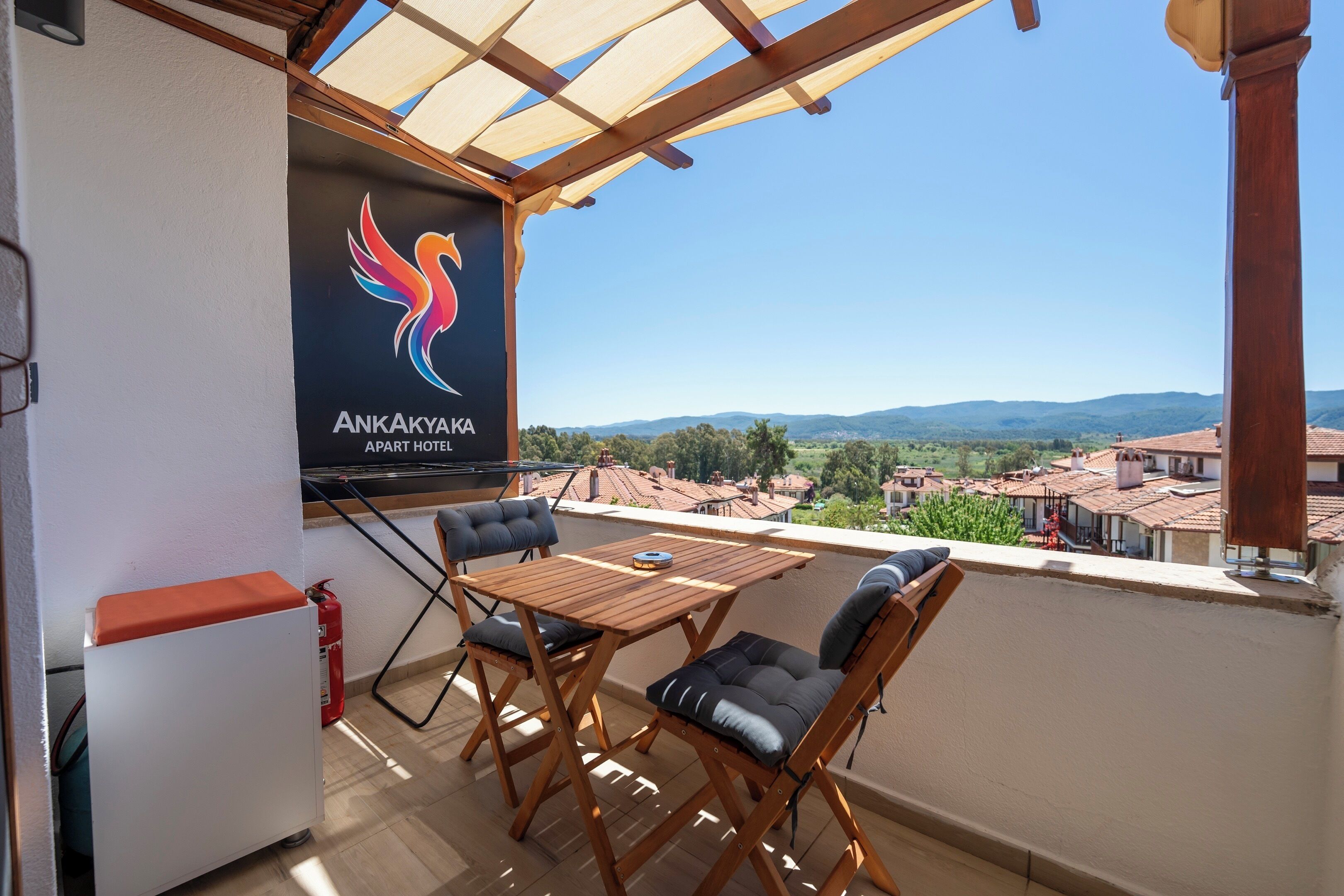 A balcony with a wooden table and chairs, a fire extinguisher, and a banner with the hotel logo.