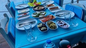 A dining table set with various dishes and drinks on a boat, with a river and another boat in the background. - Ankakyaka Apart Hotel (Ula)