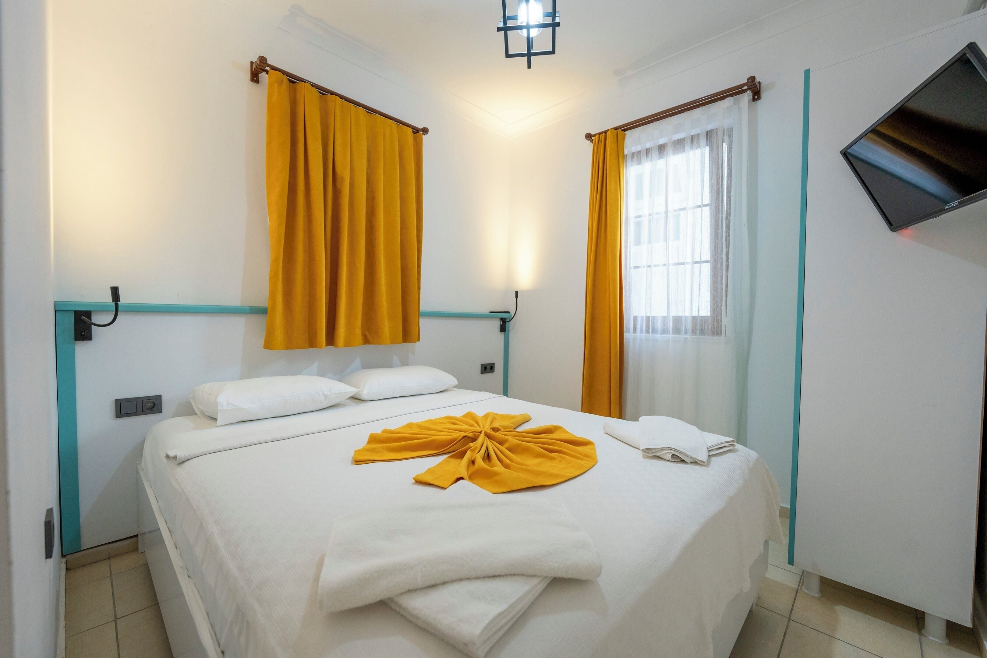 Habitación de hotel con cama, cortinas, televisor y lámpara fijada a la pared.