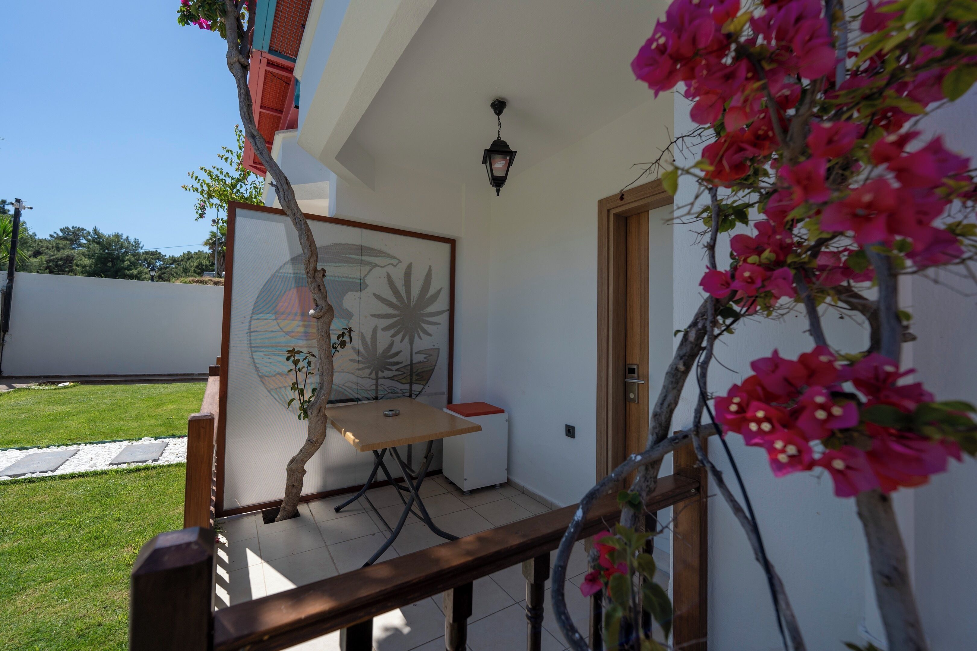 Un patio con mesa y sillas, un pequeño jardín y una puerta que da al interior.