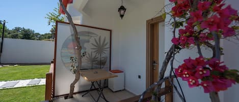 Un patio con mesa y sillas, un pequeño jardín y una puerta que da al interior.
