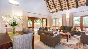 Amplia sala de estar con techo alto, una mesa de comedor con sillas, un conjunto de sofás y un ventanal con vistas al exterior.