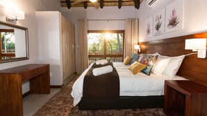 Habitación de hotel con una cama grande, un banco de madera, un ventilador de techo y una ventana con vistas a árboles.