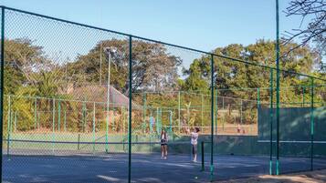 Een tennisbaan omringd door een groene hekken met bomen op de achtergrond.