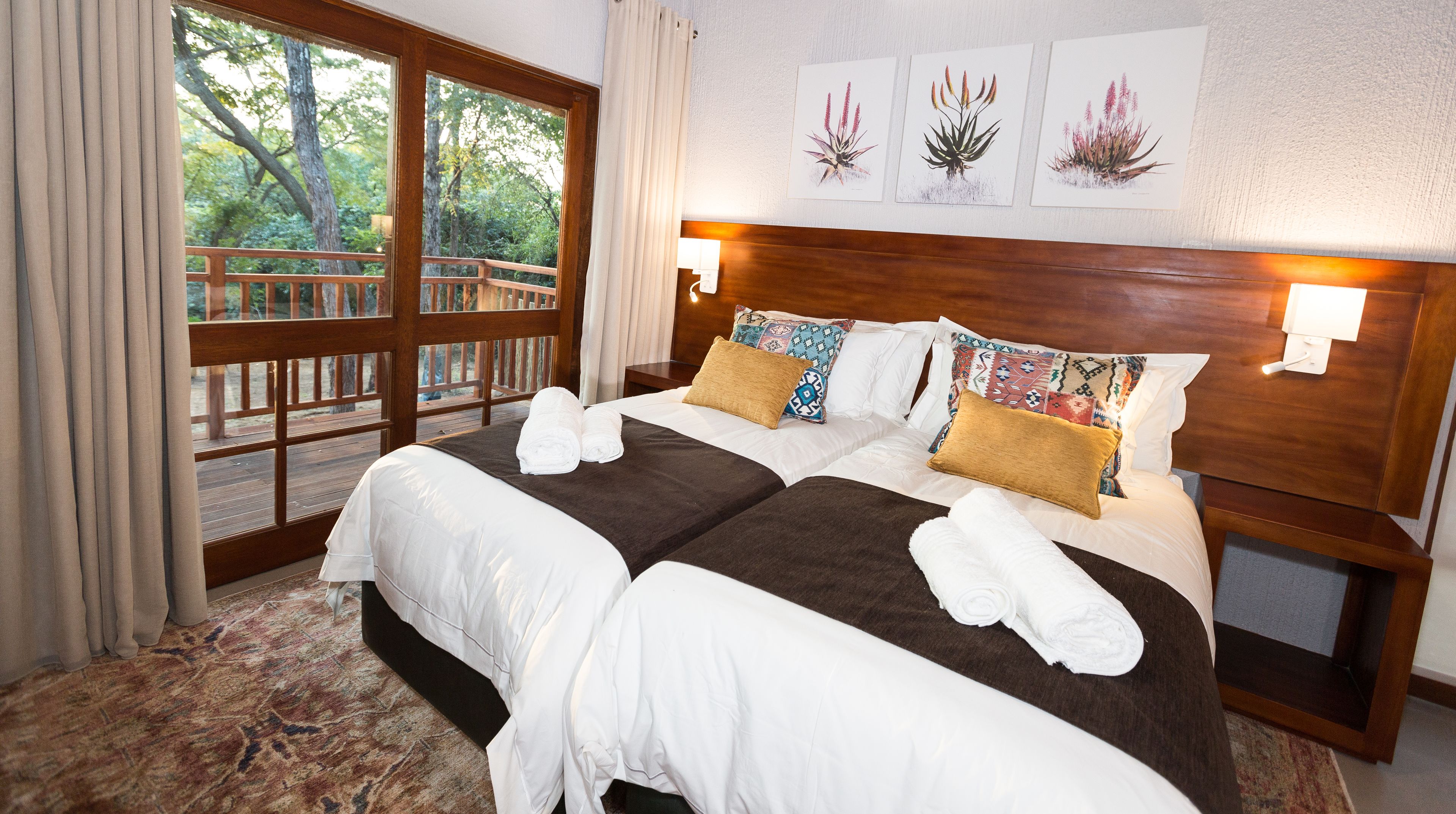 A double bed with white and brown linens, a wooden headboard, and two wall-mounted lamps.