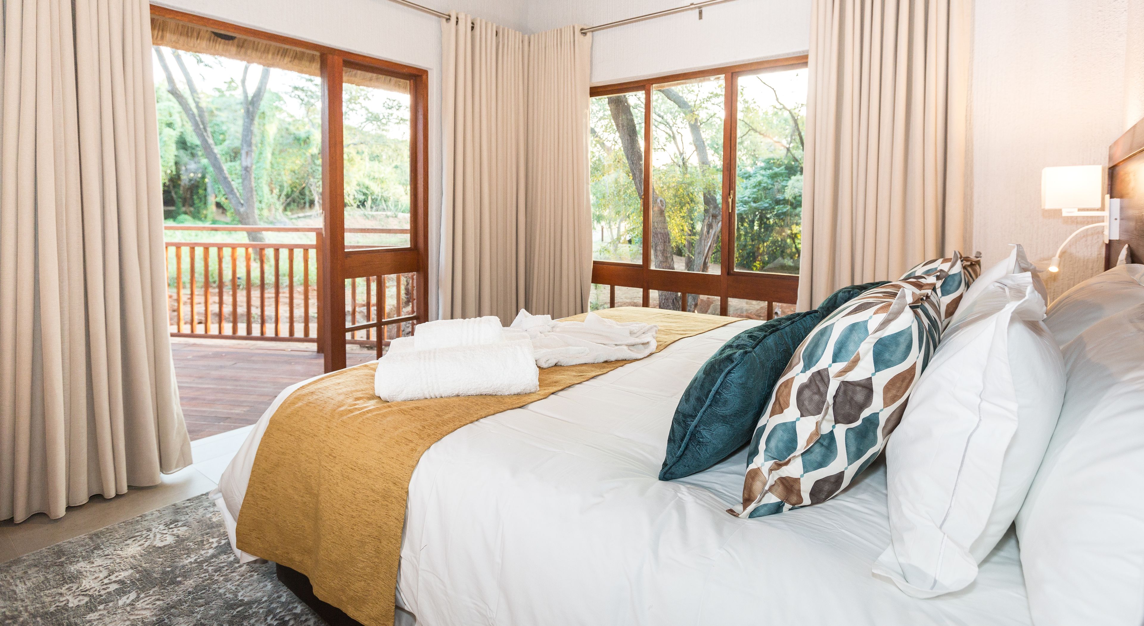 Une chambre d’hôtel avec un grand lit, une tête de lit en bois et une vue sur une terrasse et des arbres.