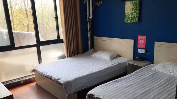 Habitación de hotel con dos camas, un ventanal grande y una pared azul.