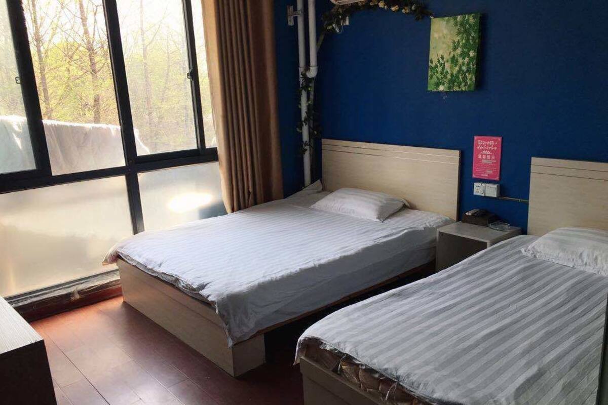 Habitación de hotel con dos camas, un ventanal grande y una pared azul.