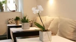 A cozy living room with a sofa, a coffee table, and a potted orchid. There is a window with plants on the sill and a wall-mounted light fixture. - DECKERT'S HOTEL AM KATHARINENSTIFT (Lutherstadt Eisleben)