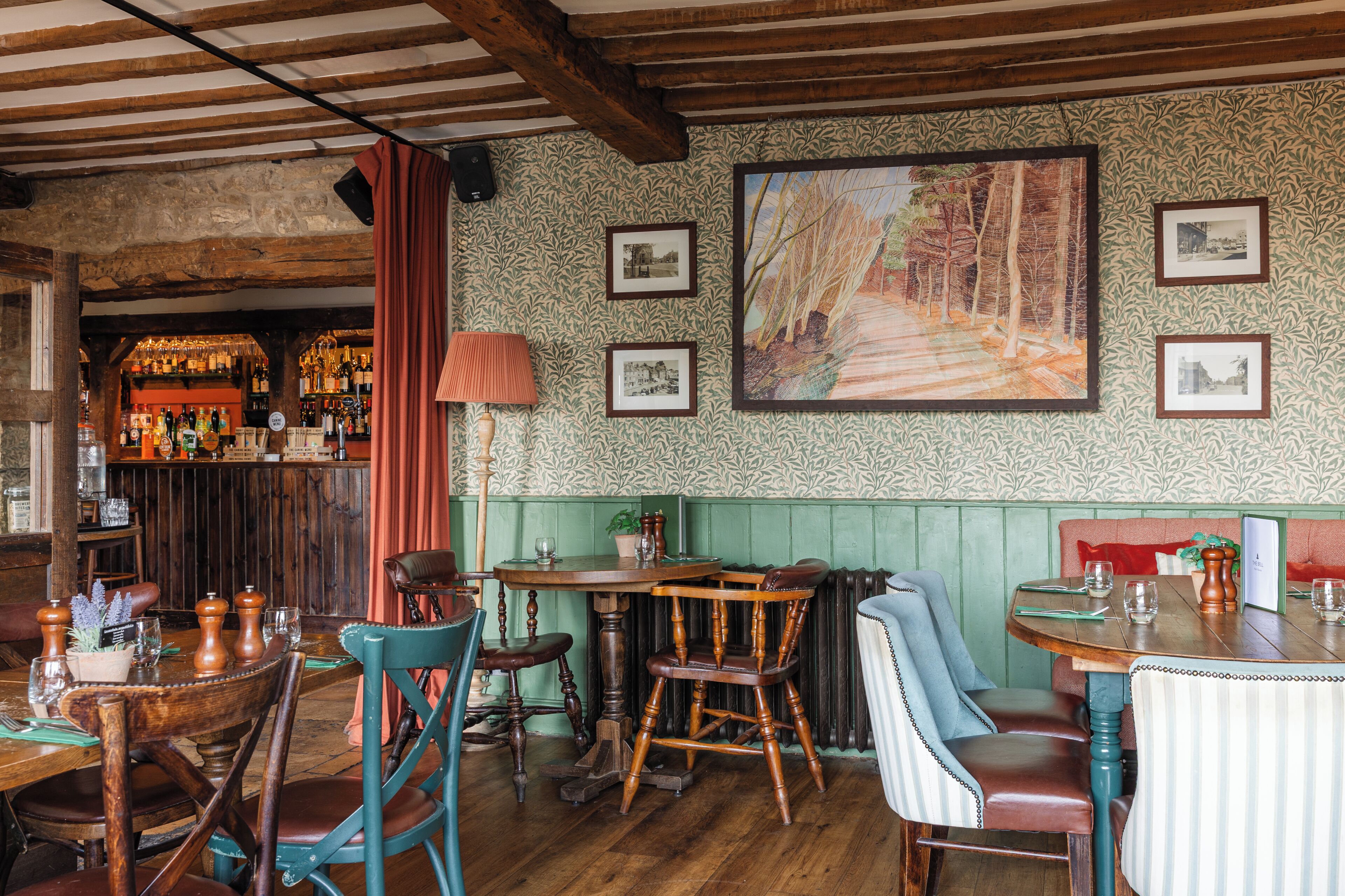 Un rincón de bar acogedor con muebles de madera, un banco tapizado de verde y un cuadro grande en la pared.