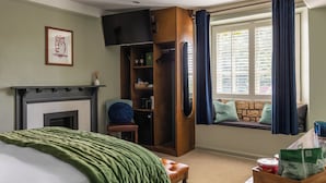 A bedroom with a fireplace, a window with curtains, a bed with a green blanket, and a wooden wardrobe.