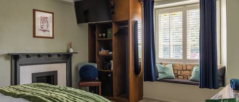Ein Schlafzimmer mit Kamin, einem fensterbepflanzten Fenster, einem Bett mit grüner Decke und einem hölzernen Kleiderschrank.