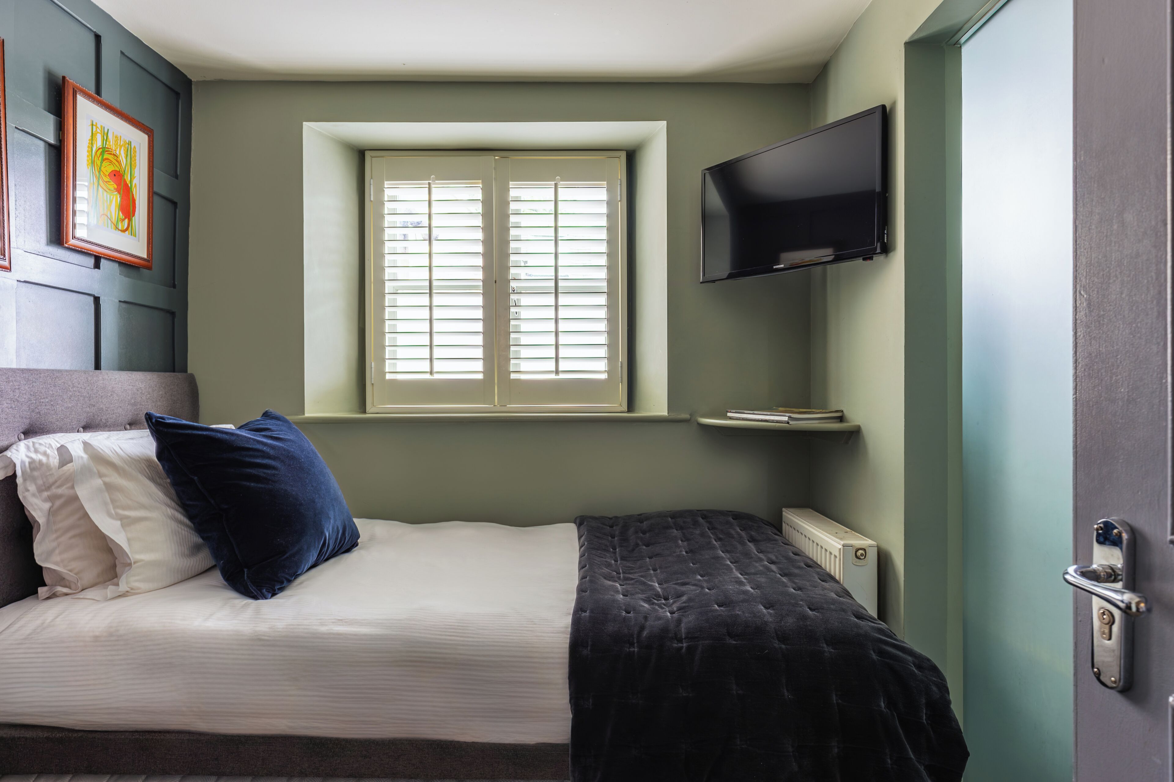 Un dormitorio con cama, ventana, televisor y radiador.