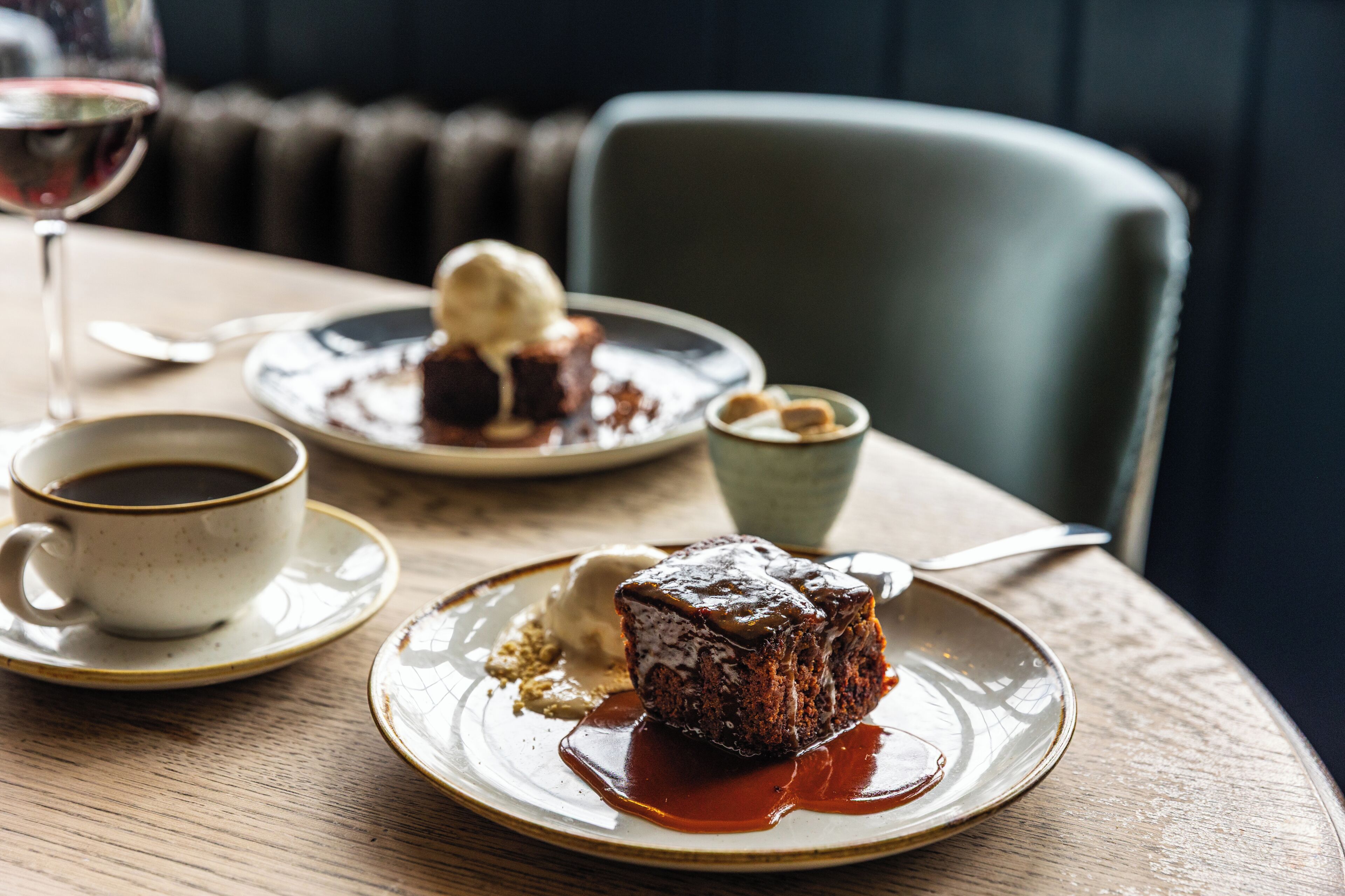 A dessert plate with a piece of cake and ice cream, a cup of coffee, and a glass of red wine on a wooden table.