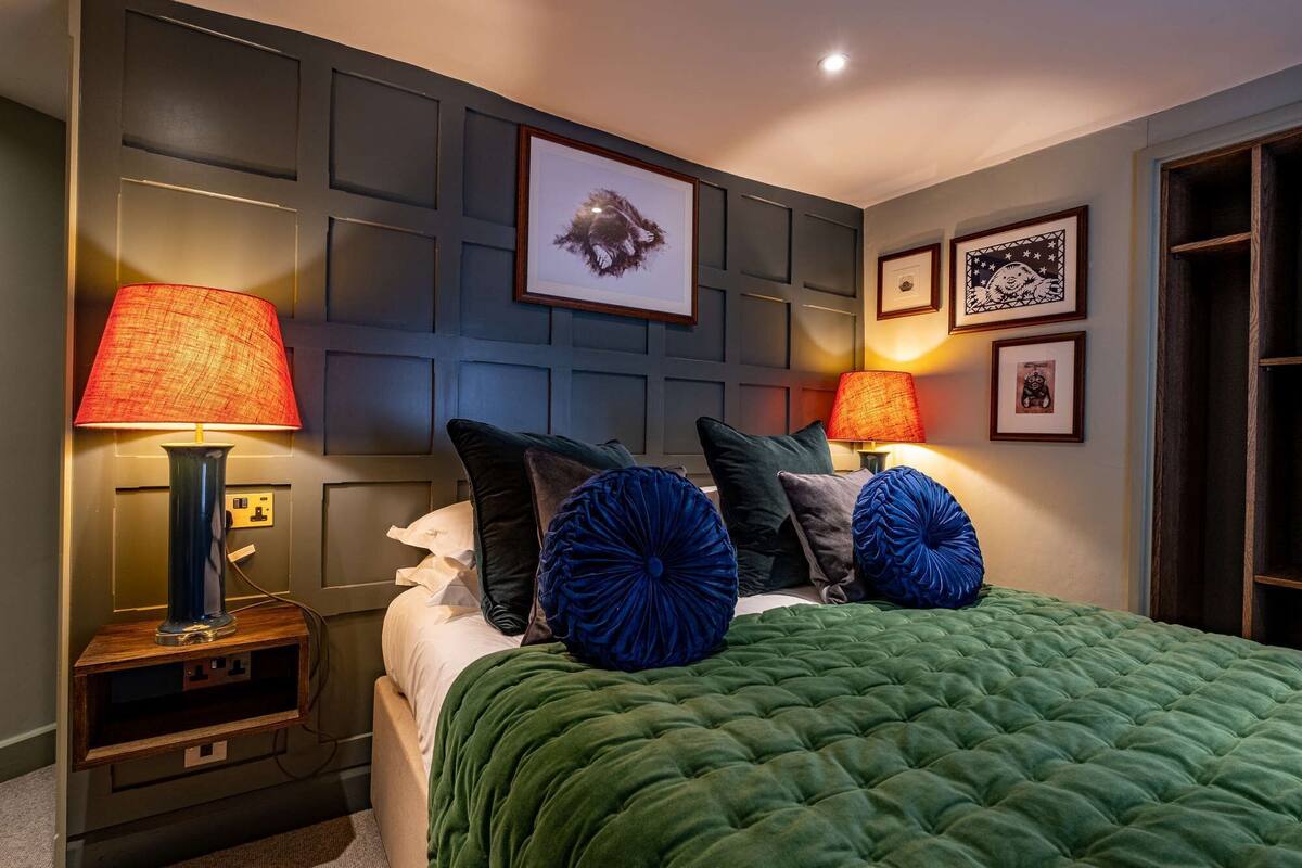 Un dormitorio ordenado con cama, dos lámparas de noche, un cuadro en la pared y una puerta.