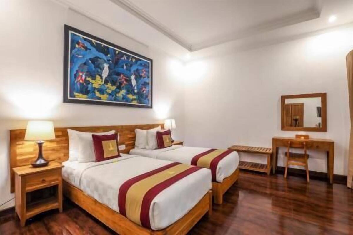 A hotel room with two beds, a desk, a chair, a painting, and a mirror.