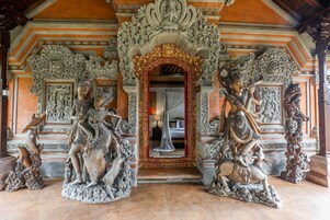 Un portal ornamentado con tallas y estatuas intrincadas, que conduce a una habitación con cama y cortina.