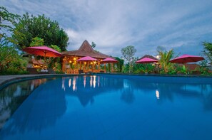 A pool area with a clear blue water surface, surrounded by lush greenery and several pink umbrellas providing shade. - Uma Dawa Resort and Spa (Ubud)