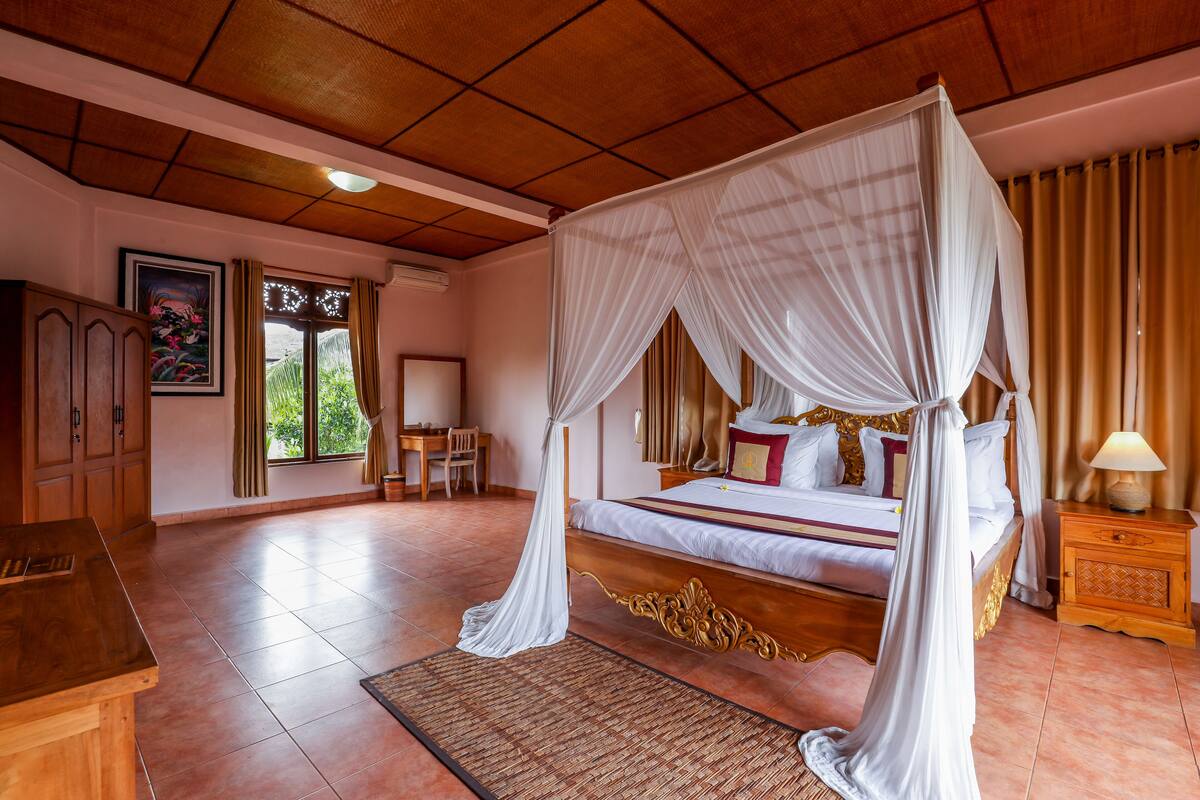 A spacious bedroom with a four-poster bed, a wooden headboard, and a nightstand with a lamp.