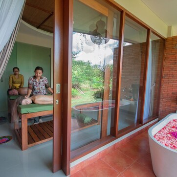 A spa area with a massage table, a glass-enclosed room, and a flower-filled bathtub.