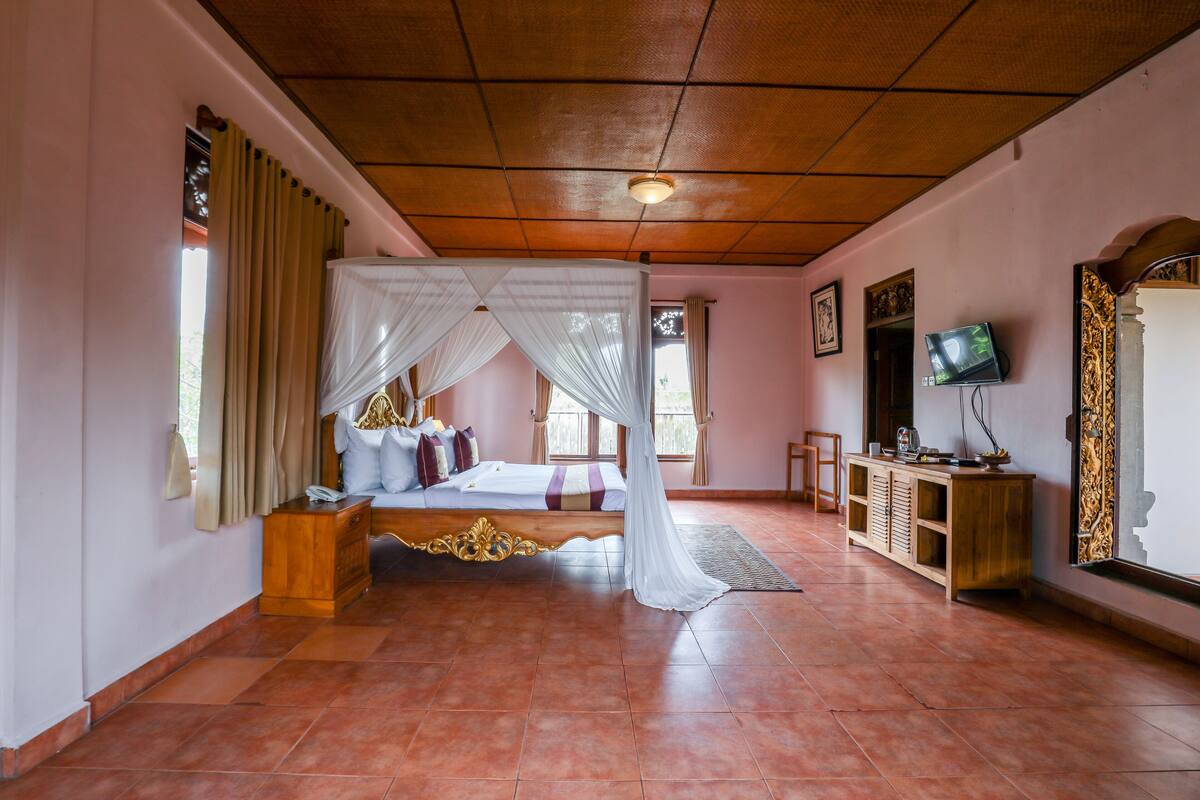 A bedroom with a four-poster bed, a wooden cabinet, a television, and a mirror.