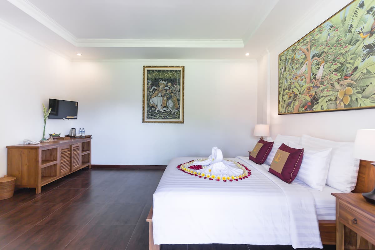 A hotel room with a large bed, a wooden side table, a TV mounted on the wall, and a painting above the bed.
