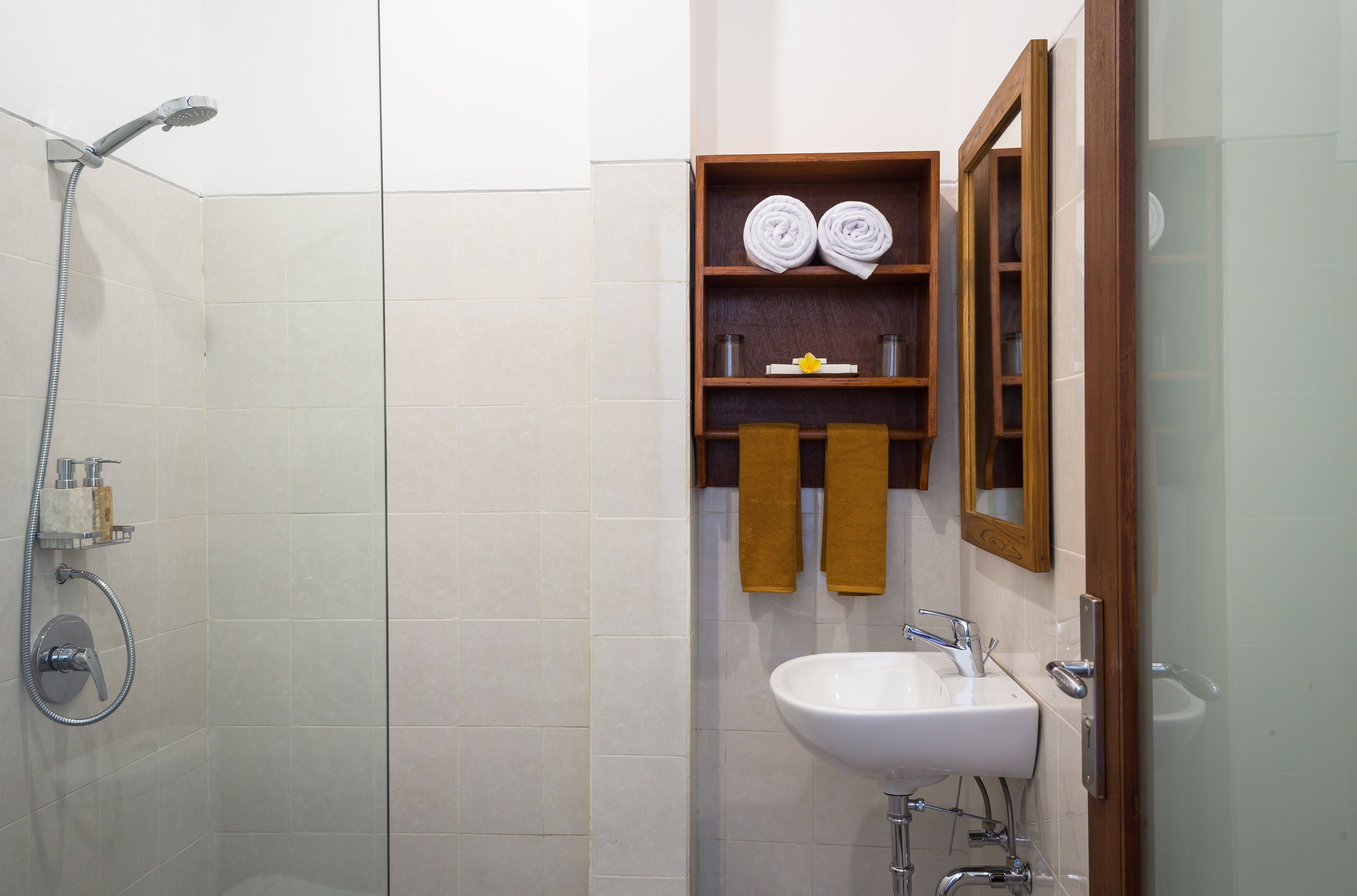 A bathroom with a shower, a sink, and a wooden shelf with towels.