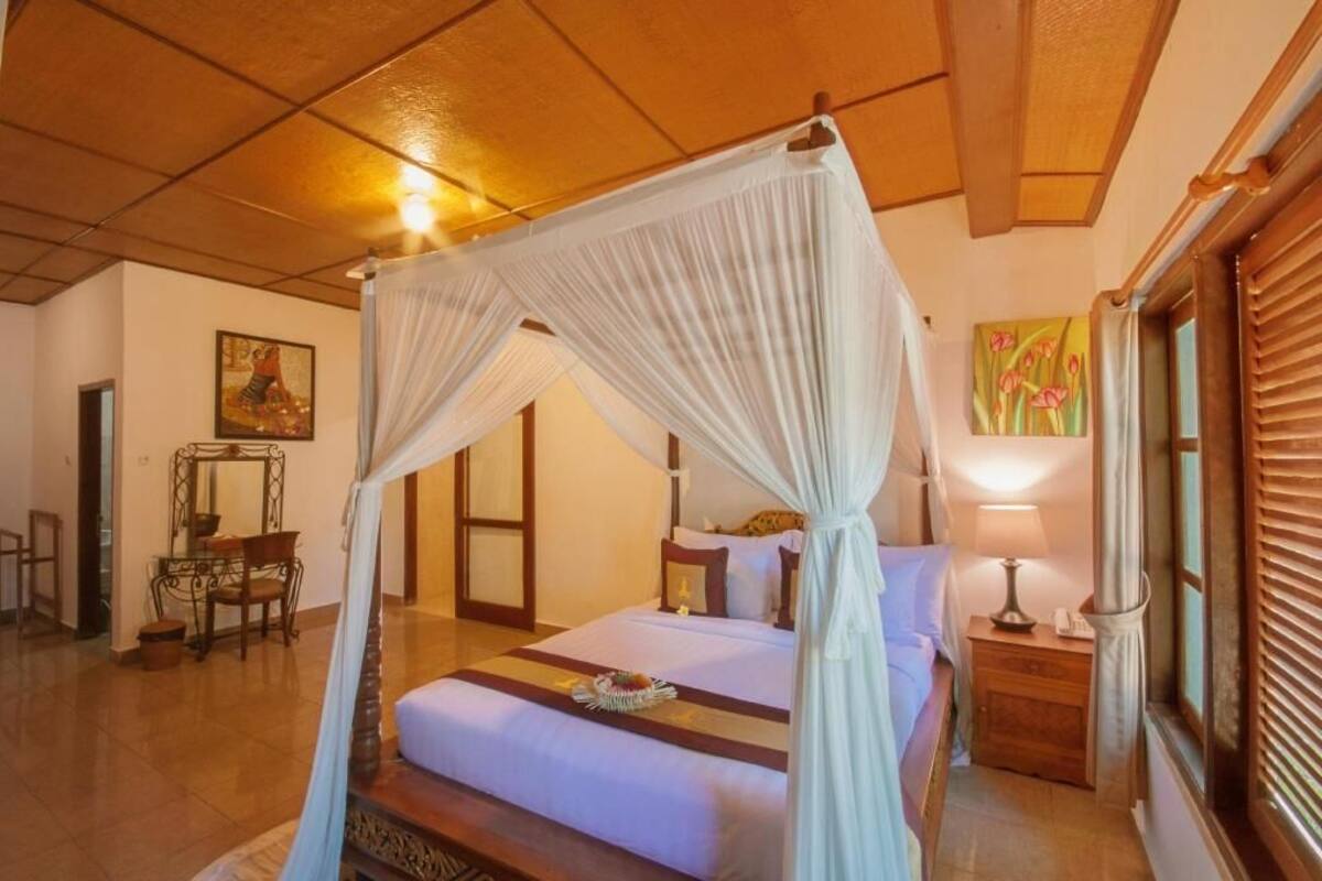 A room with a four-poster bed, a bedside table with a lamp, a mirror, and a painting on the wall.