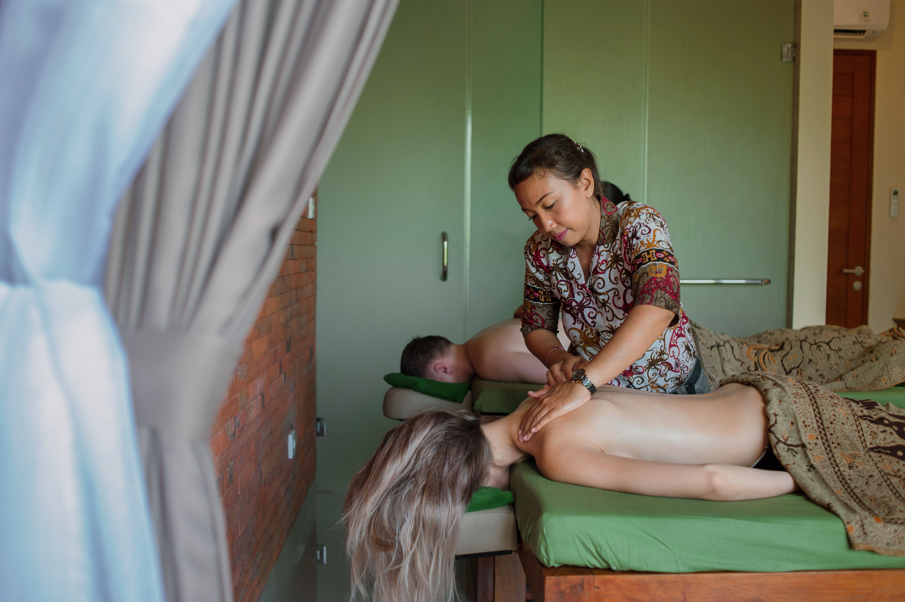 A massage therapy session in a room with a green door and a brick wall.