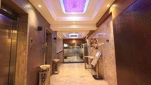 A modern elevator with a digital display, a marble-floored hallway, and a decorative wall with a circular emblem. - Hotel SN Blu (Ahmedabad)