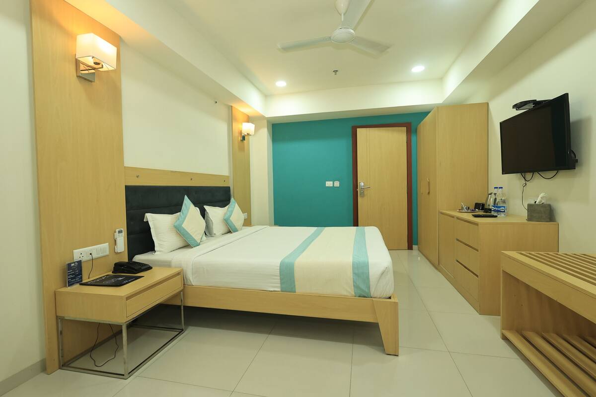 A modern hotel room with a bed, bedside table, desk, and a TV mounted on the wall.