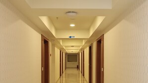 A long, well-lit hallway with a polished marble floor and wooden doors on both sides, leading to a distant room. - Hotel SN Blu (Ahmedabad)