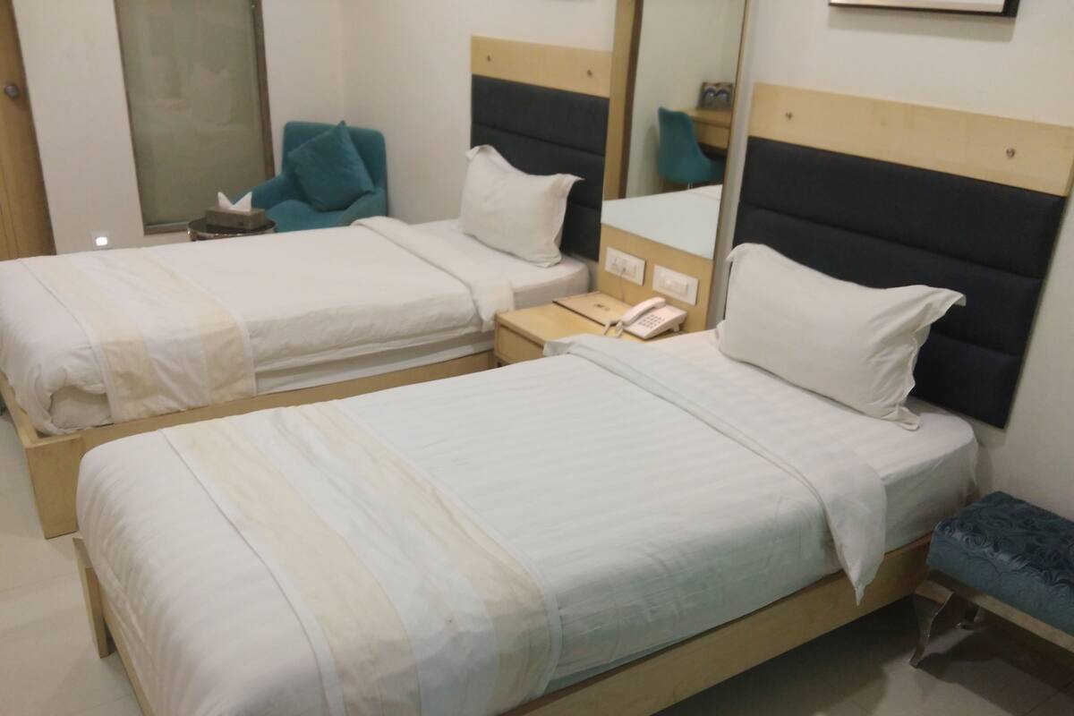 A hotel room with two beds, a bedside table with a phone, a mirror, and a small bench.