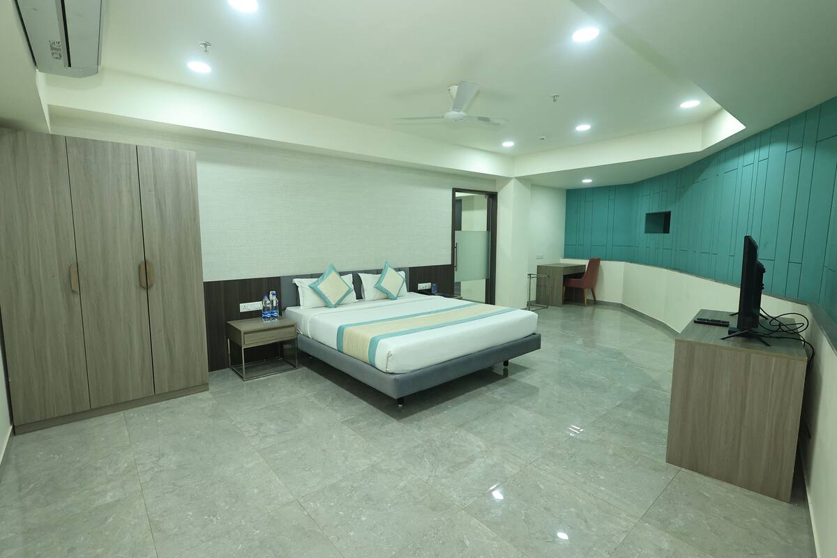 A modern hotel room with a large bed, a desk, a wardrobe, and a television.