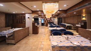 A restaurant with booths and tables, a chandelier, and a counter. - Hotel SN Blu (Ahmedabad)