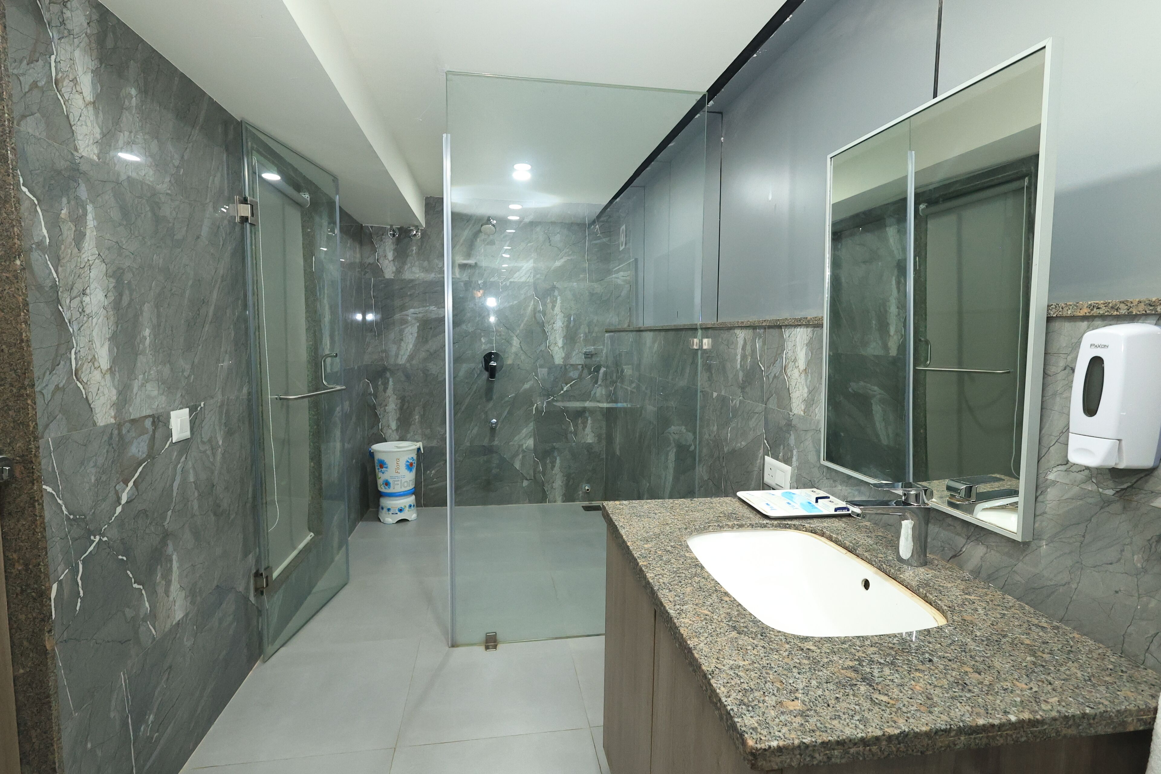 Un baño moderno con lavamanos de granito, cabina de ducha de vidrio y pared de mármol.