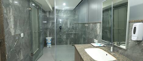 Un baño moderno con lavamanos de granito, cabina de ducha de vidrio y pared de mármol.