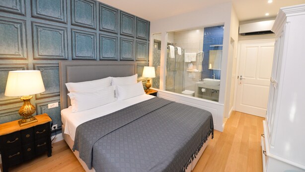 A bedroom with a large bed, two bedside tables with lamps, a glass shower enclosure, and a white wardrobe. - The Duke Luxury Rooms (Split)
