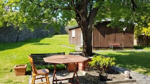 A patio with a wooden table and chairs, a stone wall, and a small shed in a grassy yard. - Burntisland House (Burntisland)