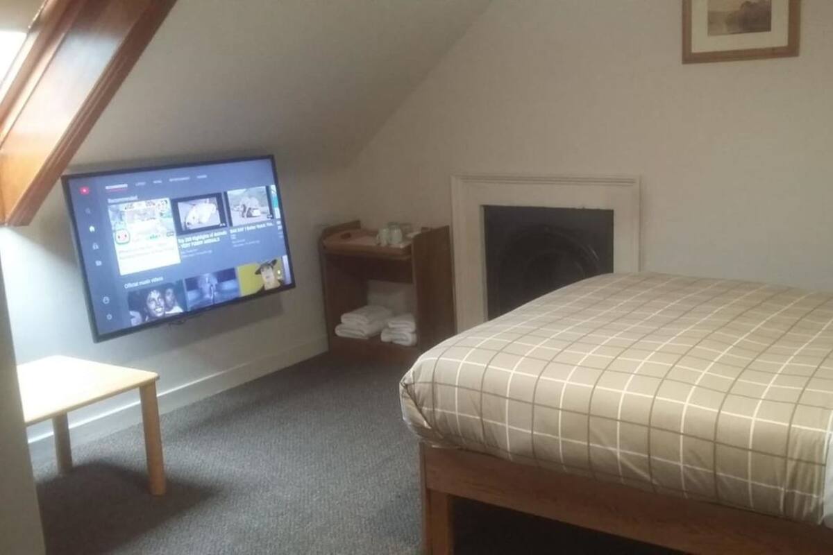 Ein Schlafzimmer mit Bett, Wandfernseher, einem kleinen Tisch und Kamin.