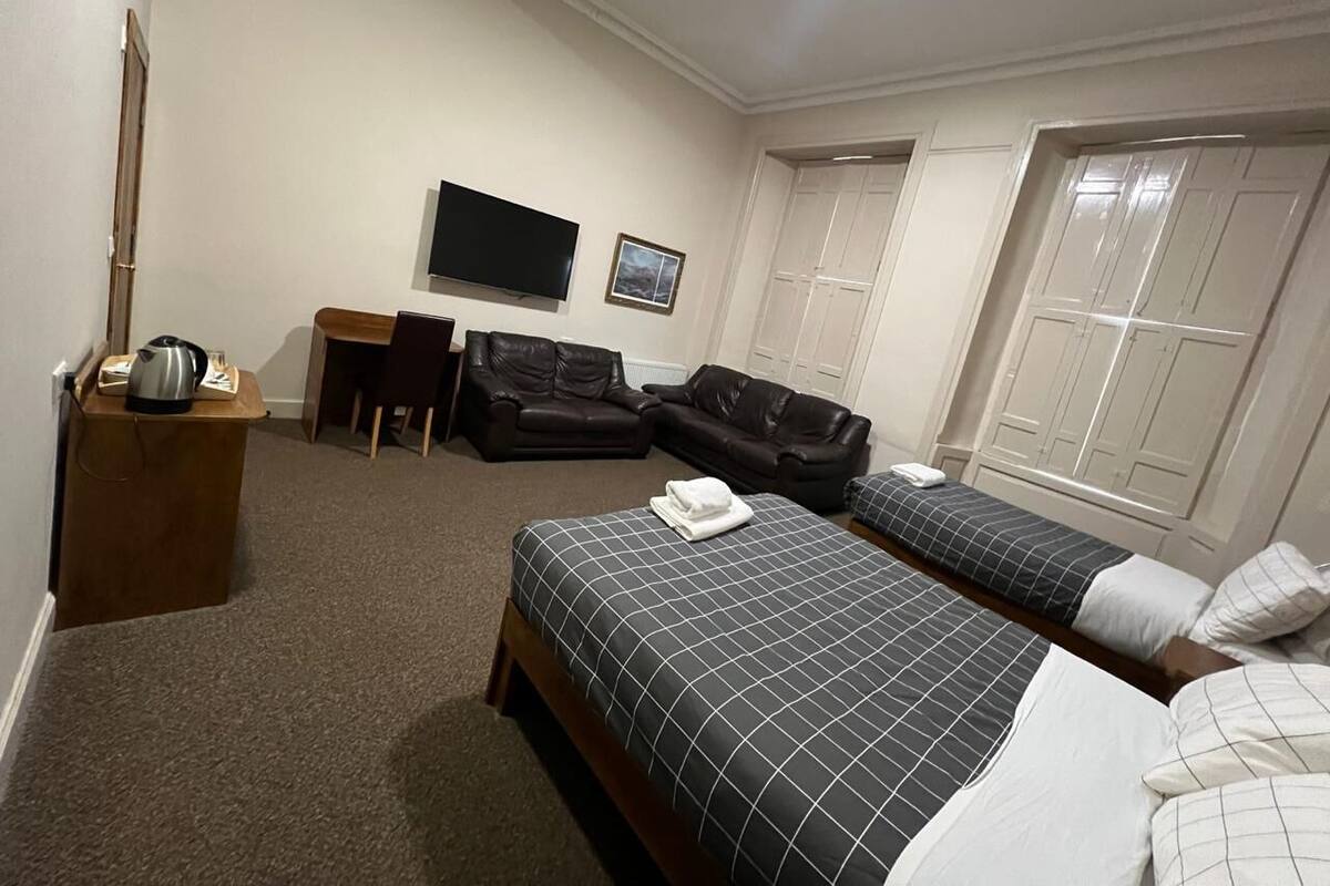 Ein Hotelzimmer mit zwei Betten, einem Fernseher, einem Schreibtisch, einem Sessel und einem Fenster.