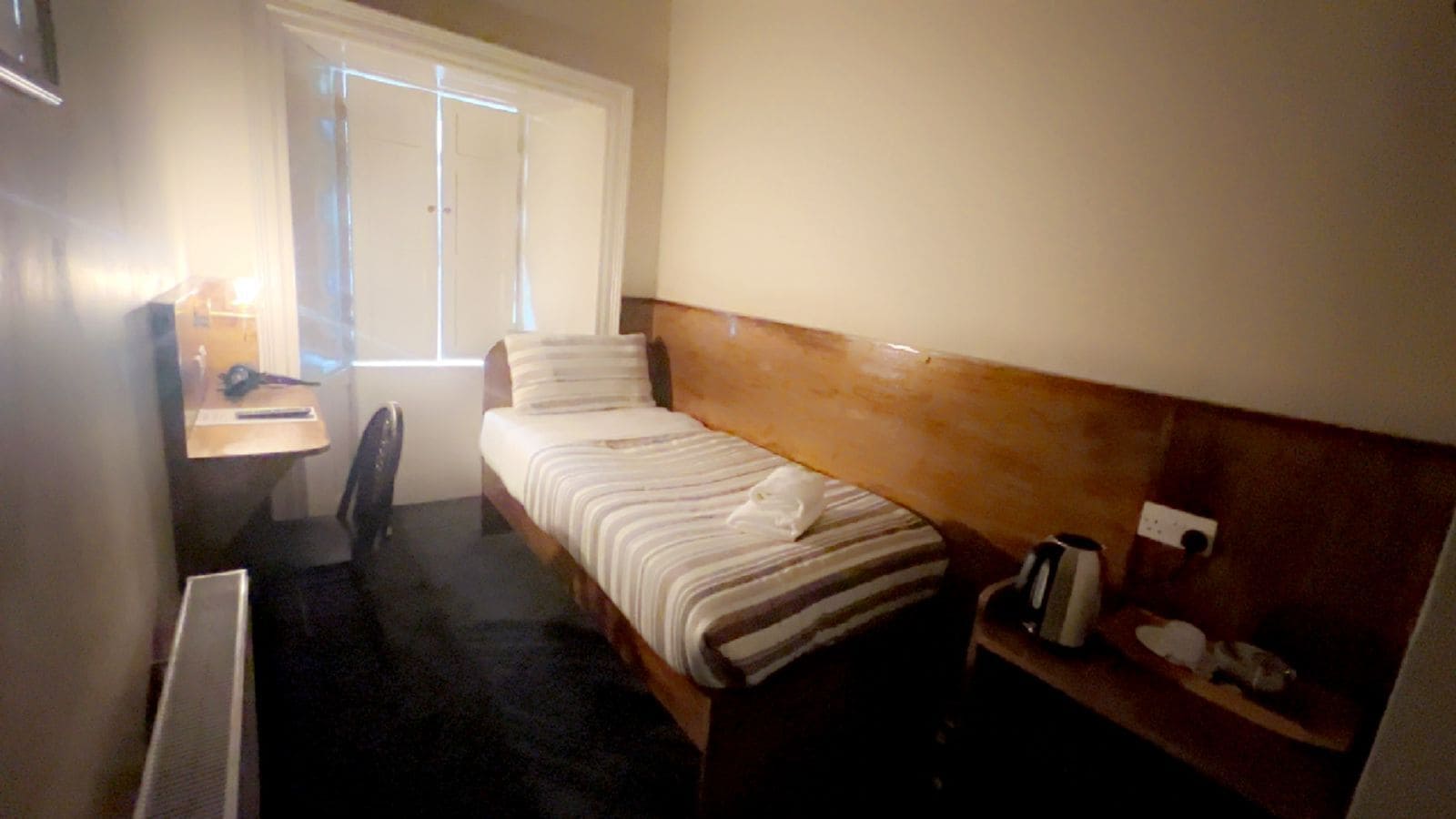 A small hotel room with a bed, a desk, a chair, and a window.