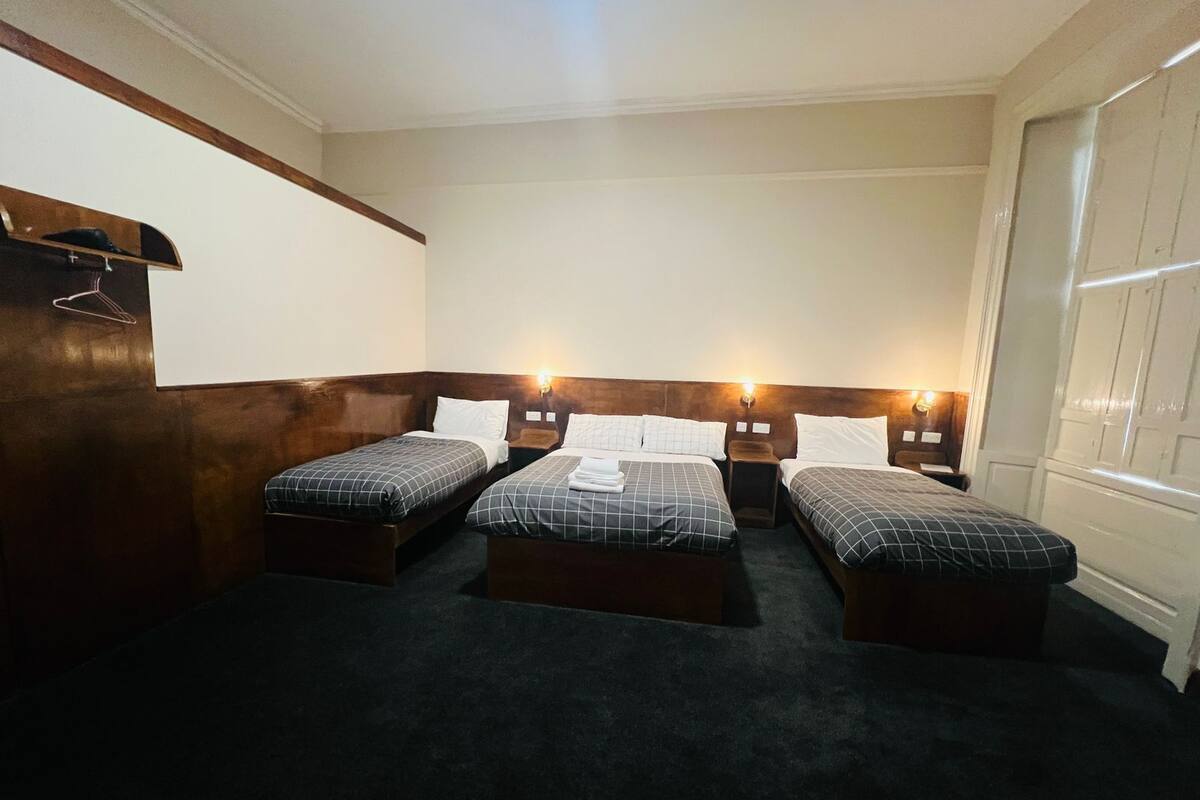 Ein Hotelzimmer mit drei Einzelbetten, Holz-Kopfteilen und Nachttischlampen.