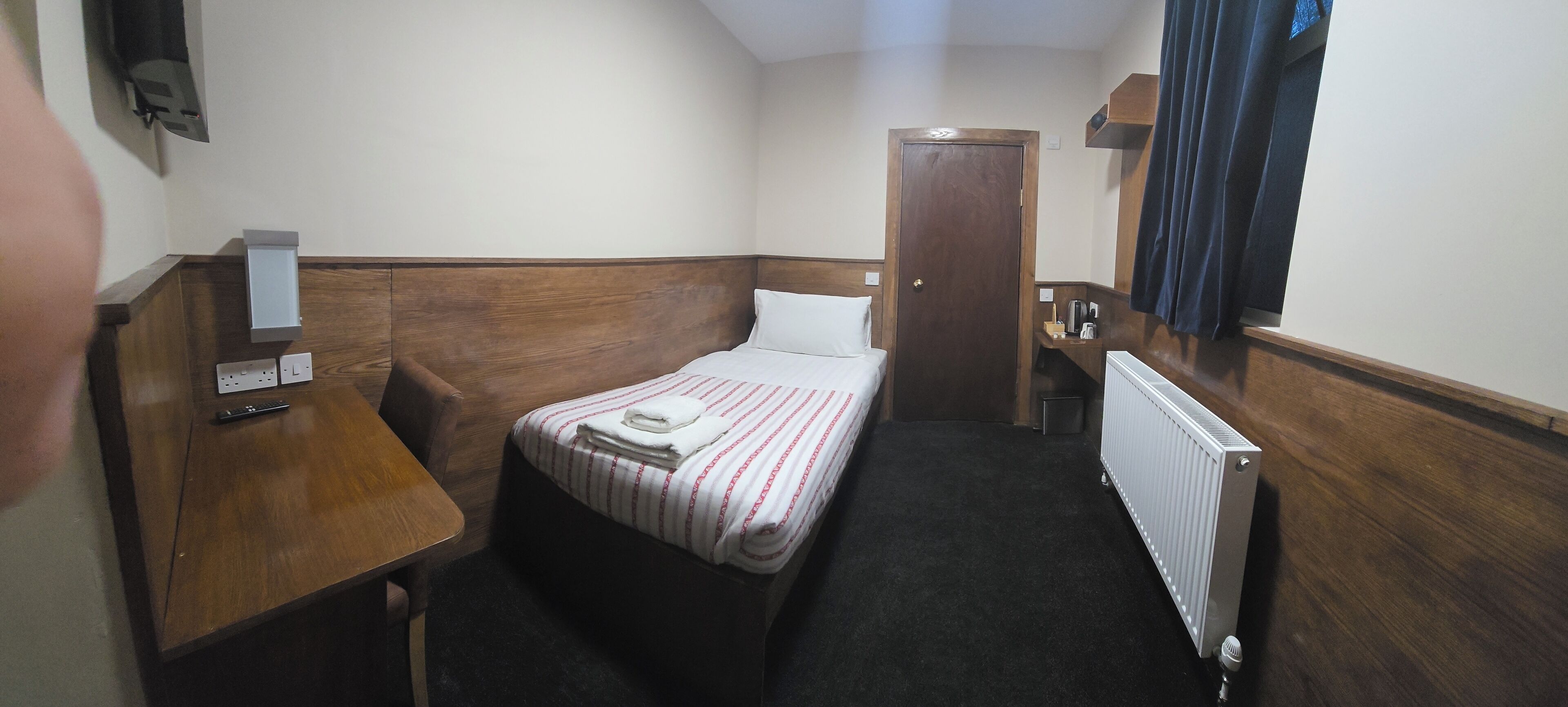 Una habitación de hotel con cama, escritorio, silla, radiador y puerta.